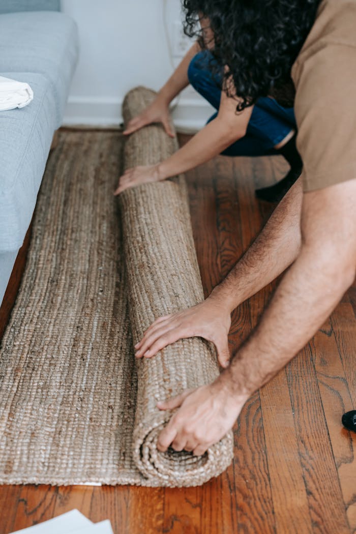 Couple rolling up a beige carpet on wooden floor, preparing for moving day.