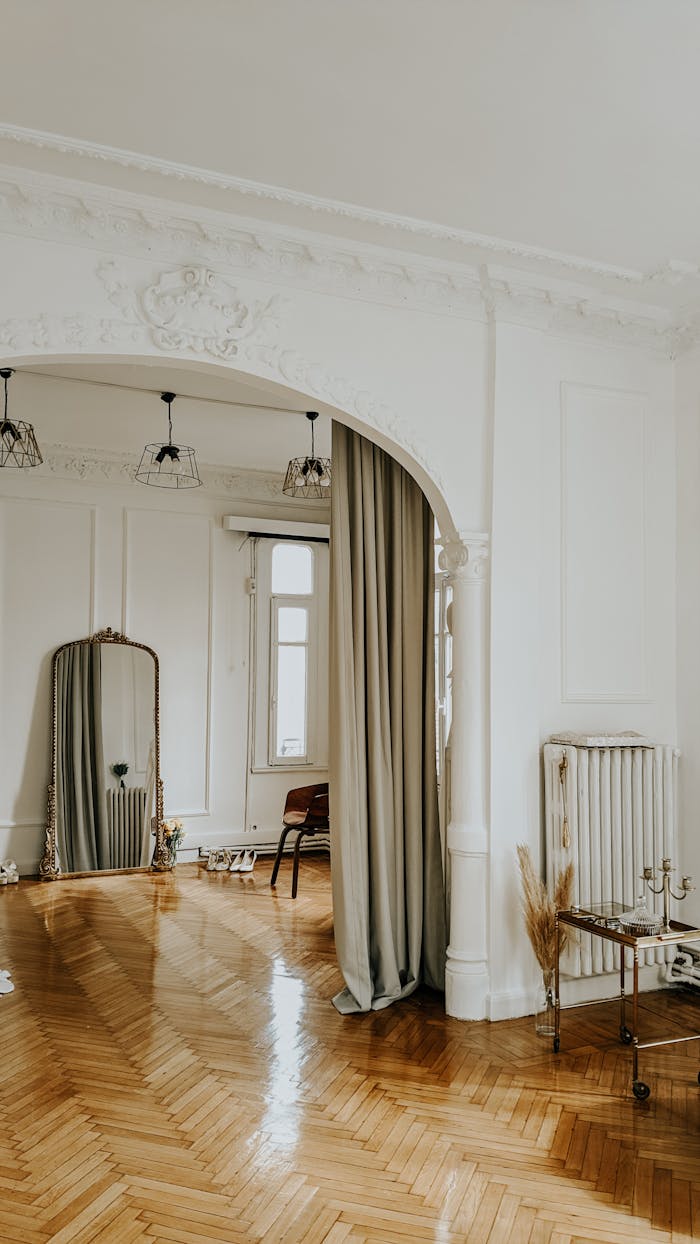 Interior of spacious light elegant house with curtain and archway near white walls with ornaments near different decorative elements and mirror near window