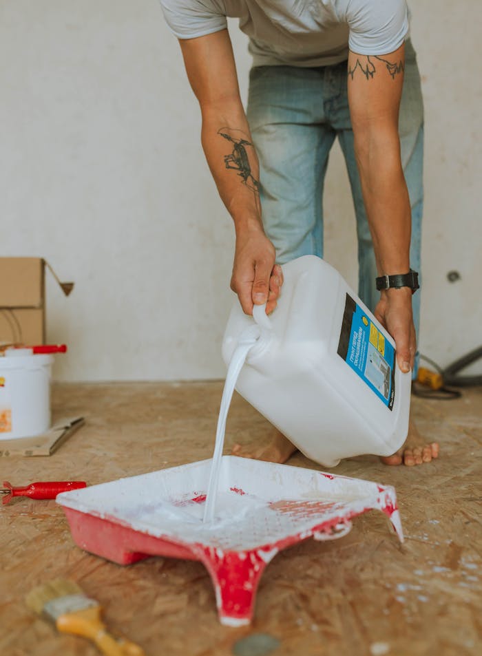 Close-up of a man pouring white paint into a tray during a home renovation indoors.